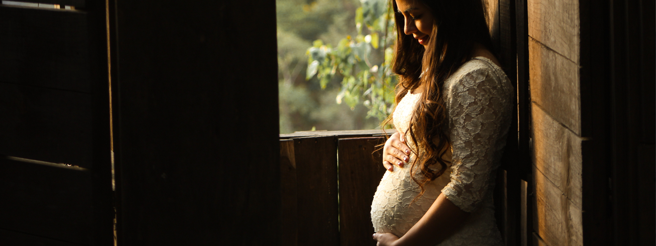 A pregnant woman standing near a window.
